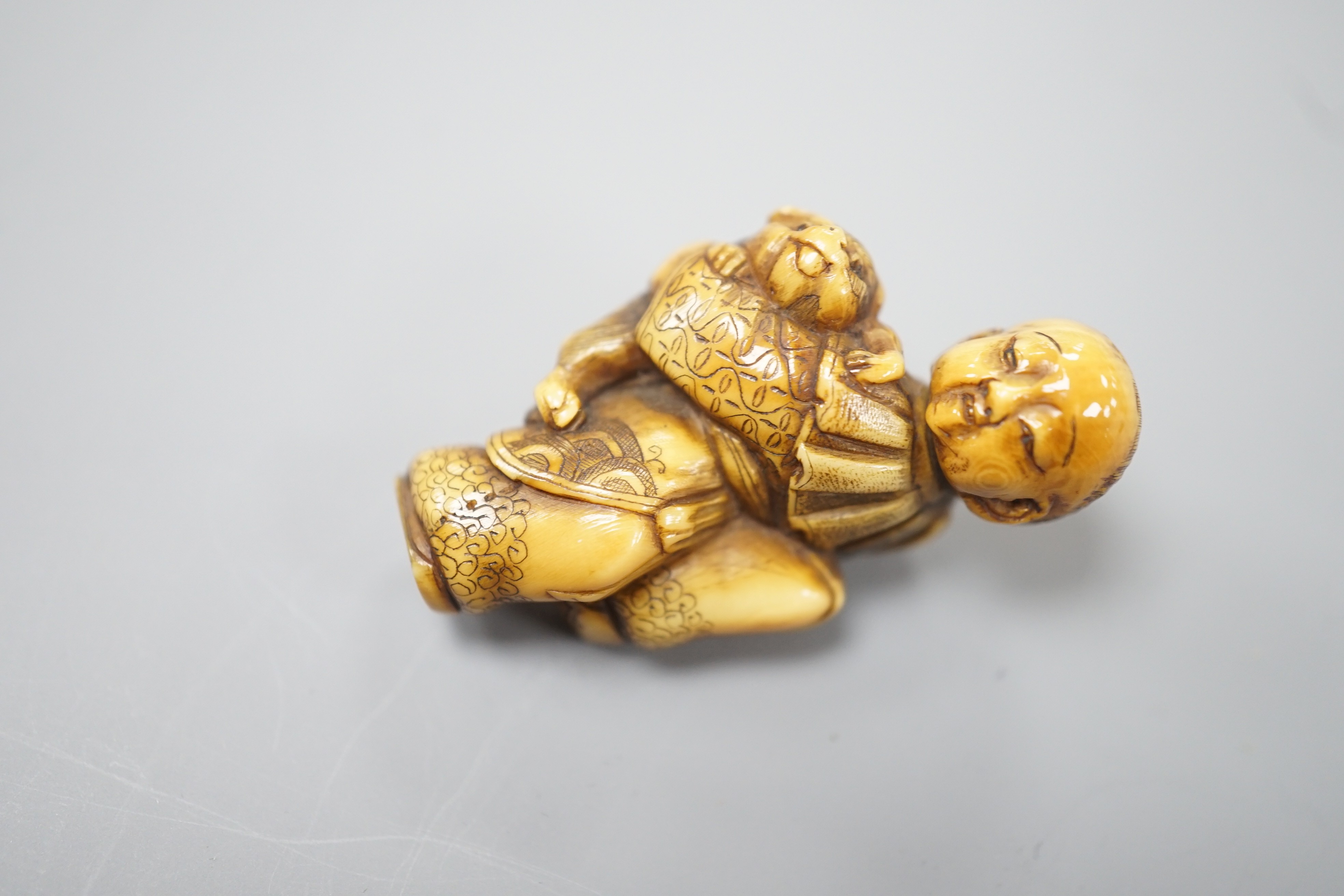 A Japanese ivory netsuke of a dog piggybacking a boy, Meiji period, 3.9cm
